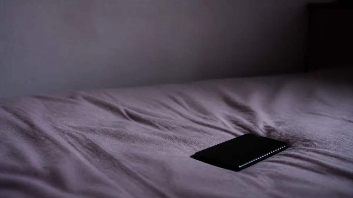 深夜のベッドに置かれたスマートフォン。返信を待つ時間のイメージ